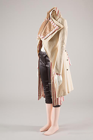 cream-colored coat with broad lapels and pink and white striped lining exposed deliberately at bottom over dark brown breeches