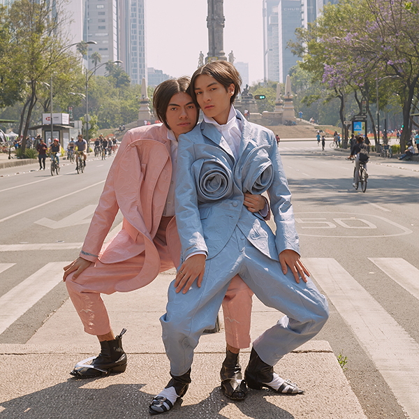 models Emiliano and Samuel posing in pastel suits in the middle of a wide city street 