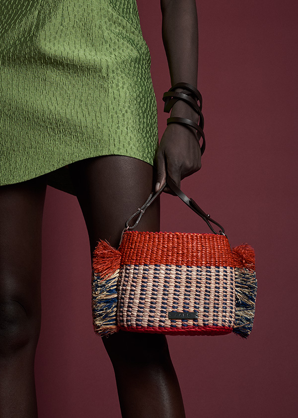 a Black woman in a green dress holding a tan woven bag