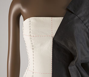 strapless oatmeal colored dress with black and red stitching and black fabric stitched to left side, draped over shoulder