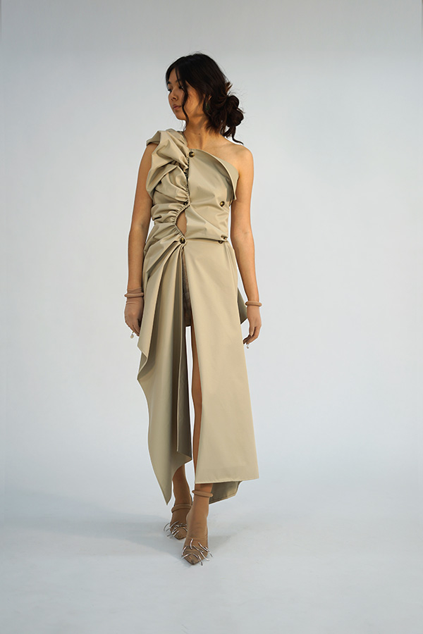 Model wearing a beige dress, designed by Yvonne Schichtel in 2021, made to look like a deconstructed, ruched trench coat. 