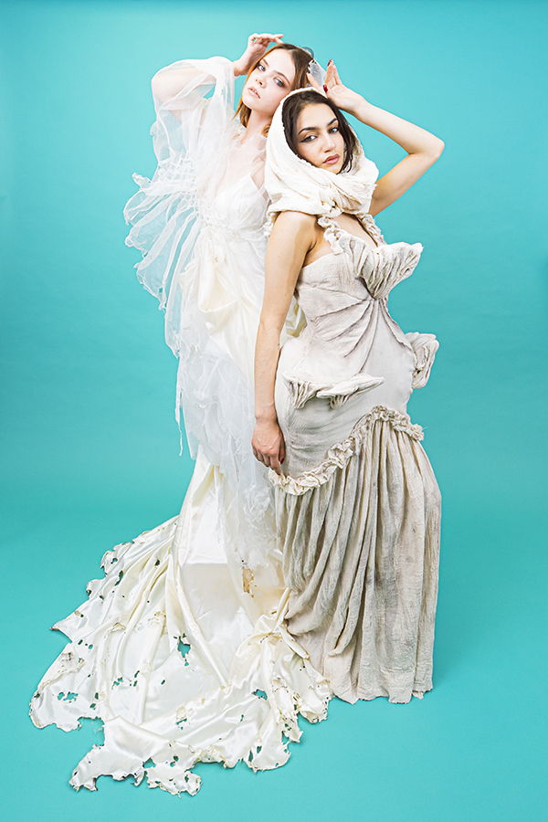 two models posing in white gowns against a bright blue backdrop