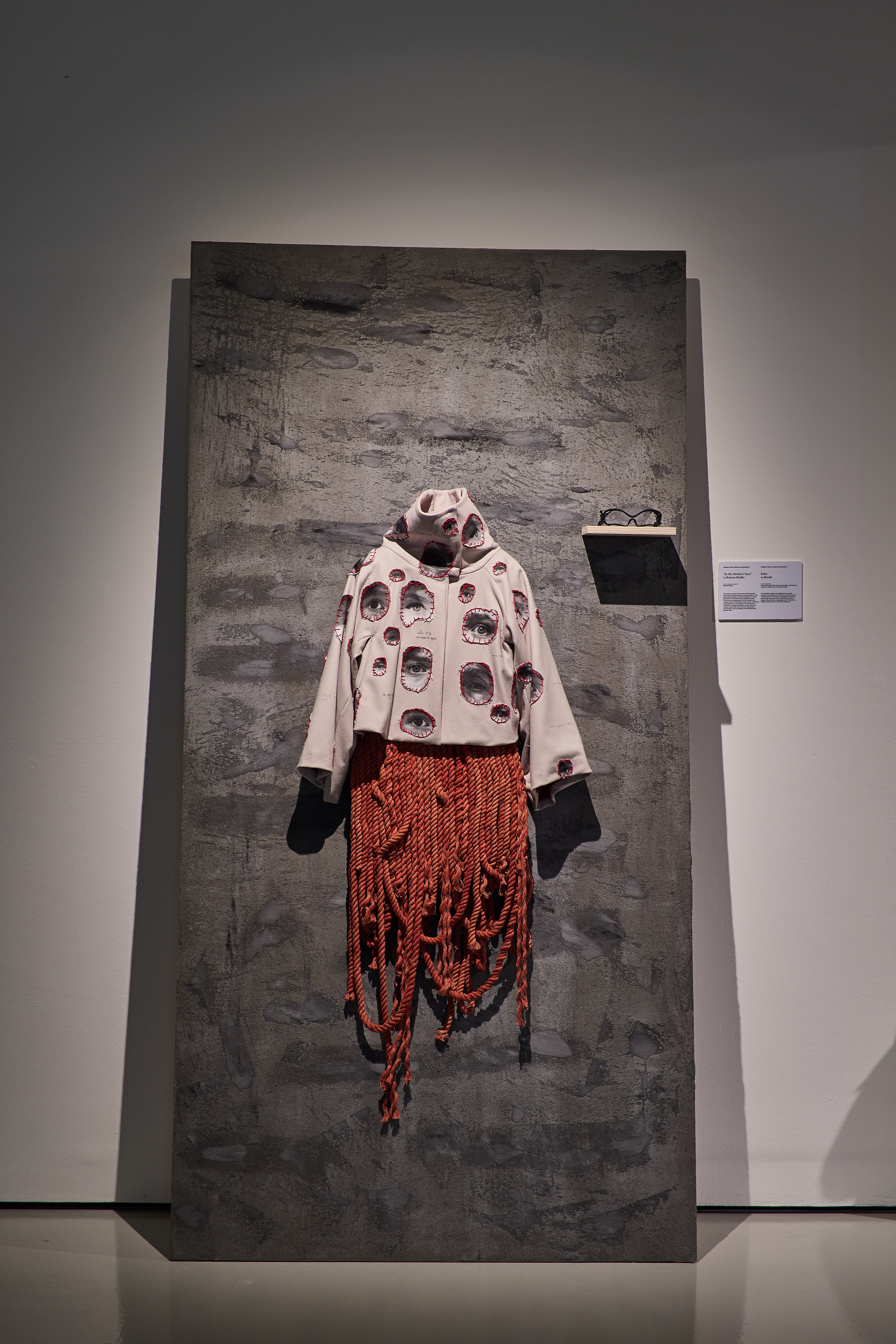 beige wide sleeved hoodie with printed eye cutouts patched on styled with a skirt made of red rope