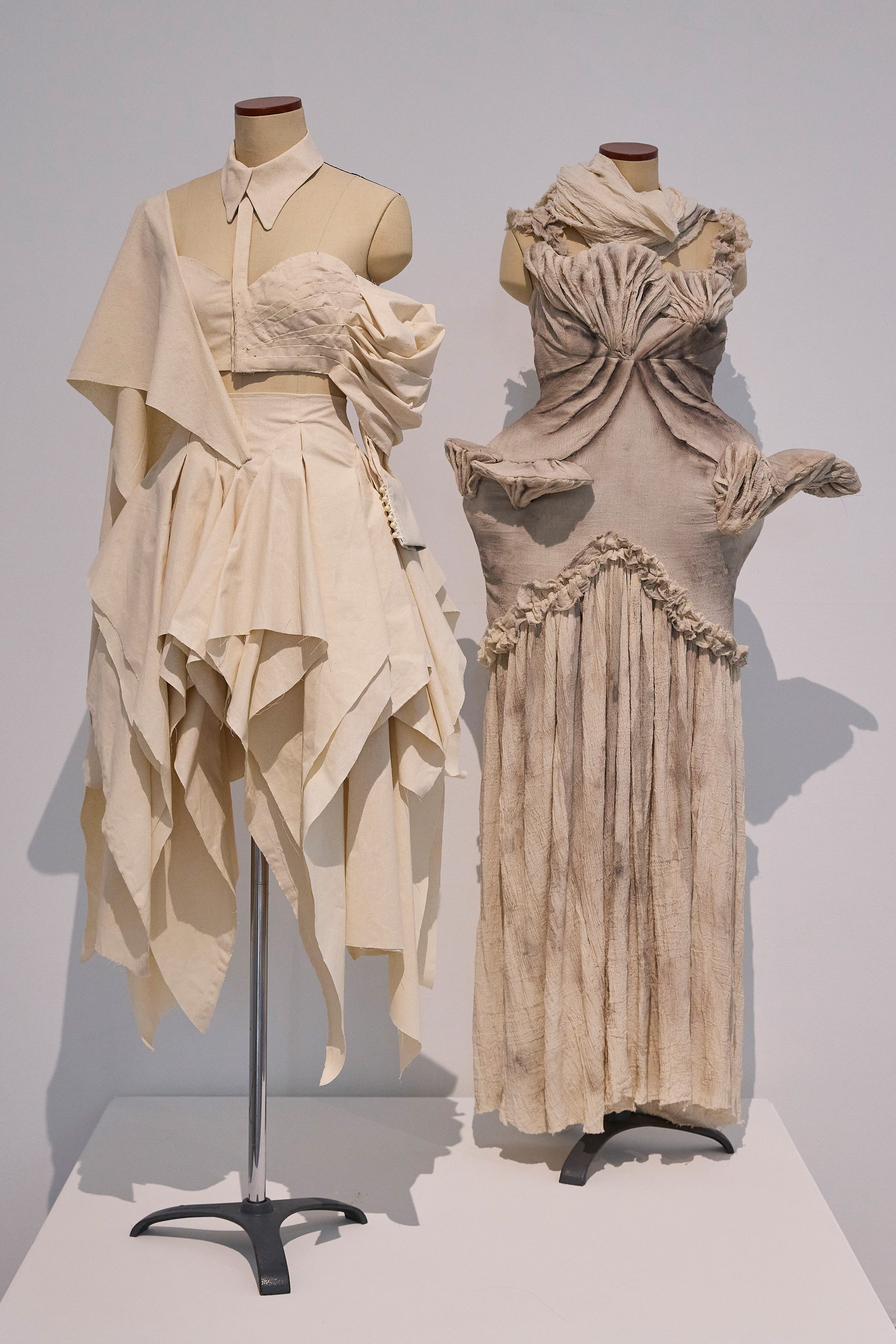 two off-white and cream dresses on mannequins in a gallery