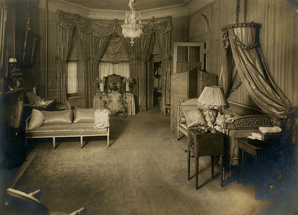 an interior room with furniture and a woman sitting in front of a vanity in the back of the room in sepia tone