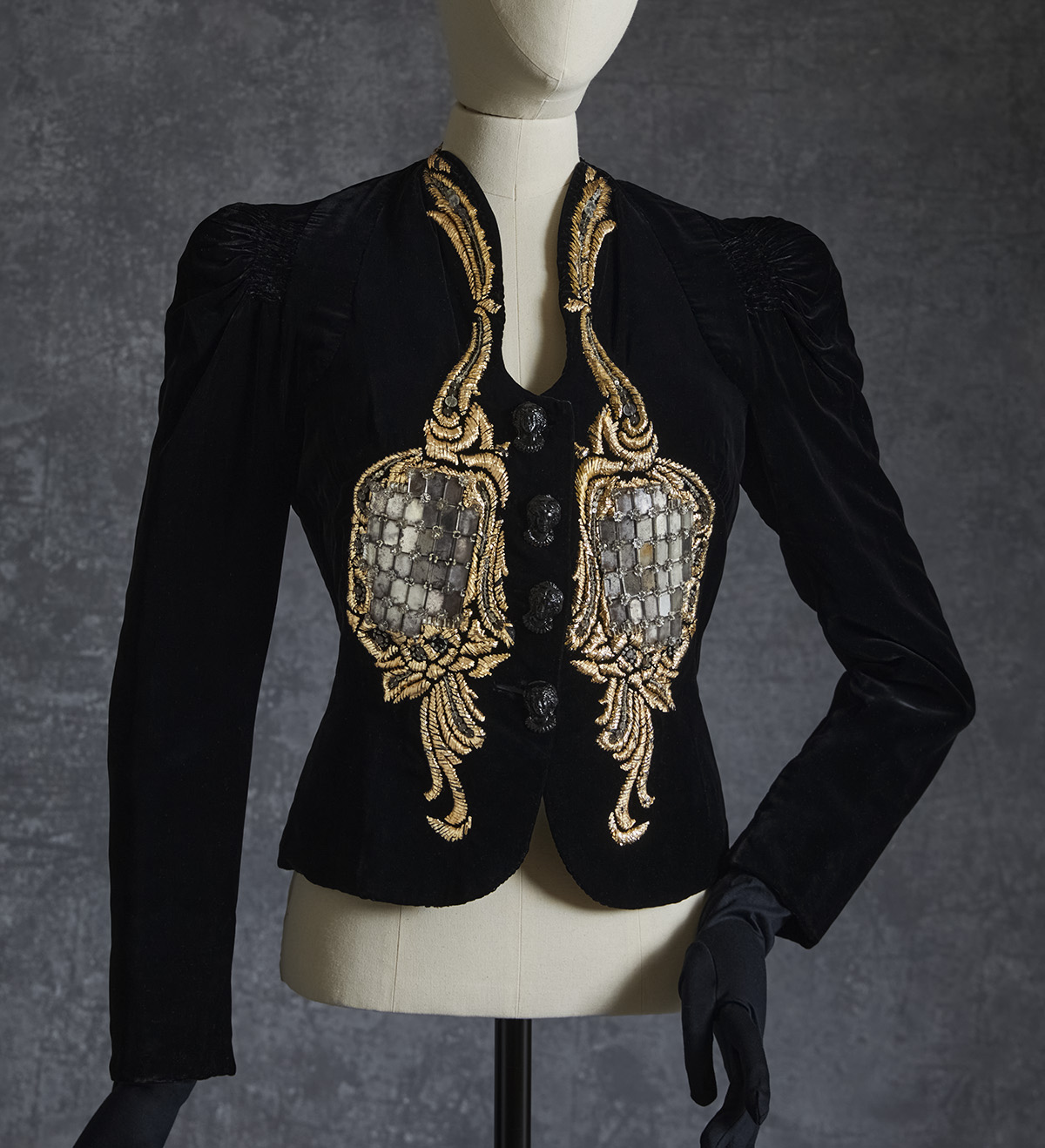 black suit jacket with gold embroidery on the front in the shape of two mirrored bird-like motifs, filled with a grid of silver reflective discs