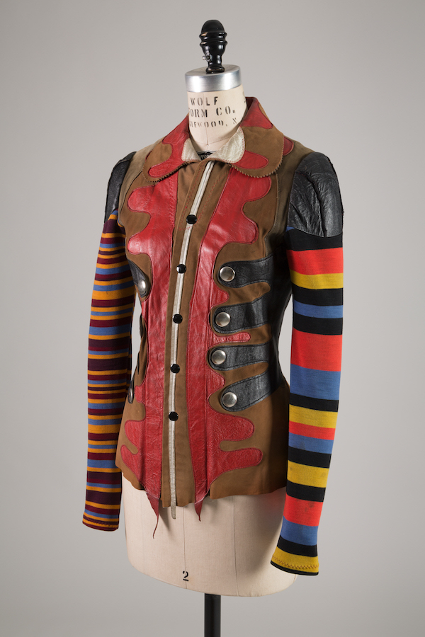 Assymetrical leather jacket with abstract design of tan, red and black and white pieces, with multicolor knit sleeves