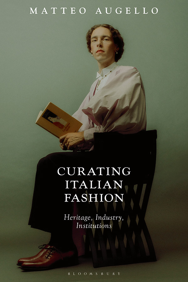 "Curating Italian Fashion" book cover with a man wearing a white voluminous top while sitting on a chair and holding a book