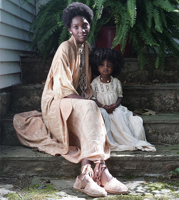 A woman wearing a cream, hand-dyed ensemble sitting with a young child wearing a white dress