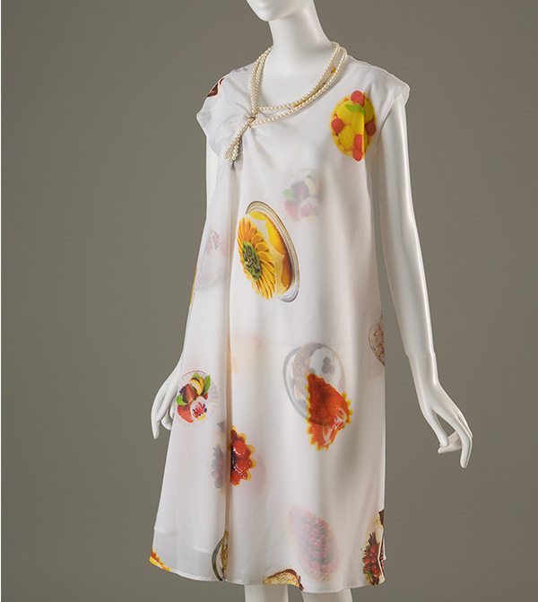 Sheer white double layer A-line dress printed with photographs of desserts and pastries with asymmetrical neckline trimmed with pearl strands
