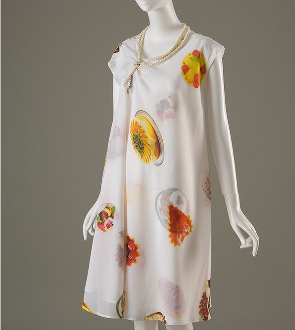 Sheer white double layer A-line dress printed with photographs of desserts and pastries with asymmetrical neckline trimmed with pearl strands