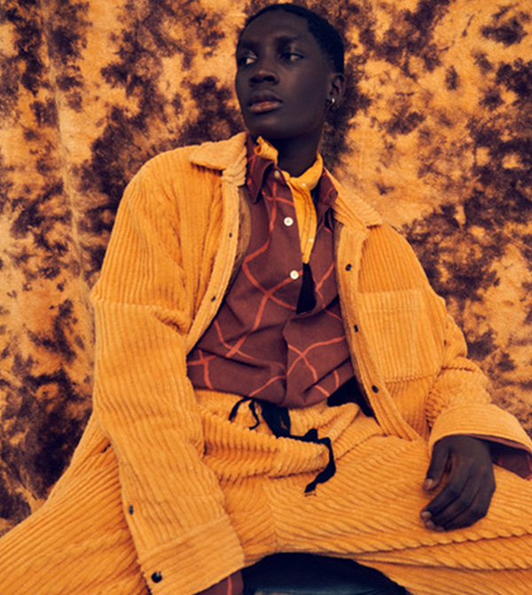 Model wearing yellow ochre corduroy ensemble with brown button down top