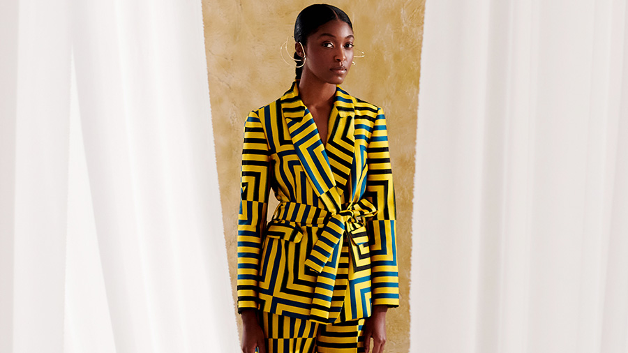 woman waering a multi colored patterned suit in between white curtains