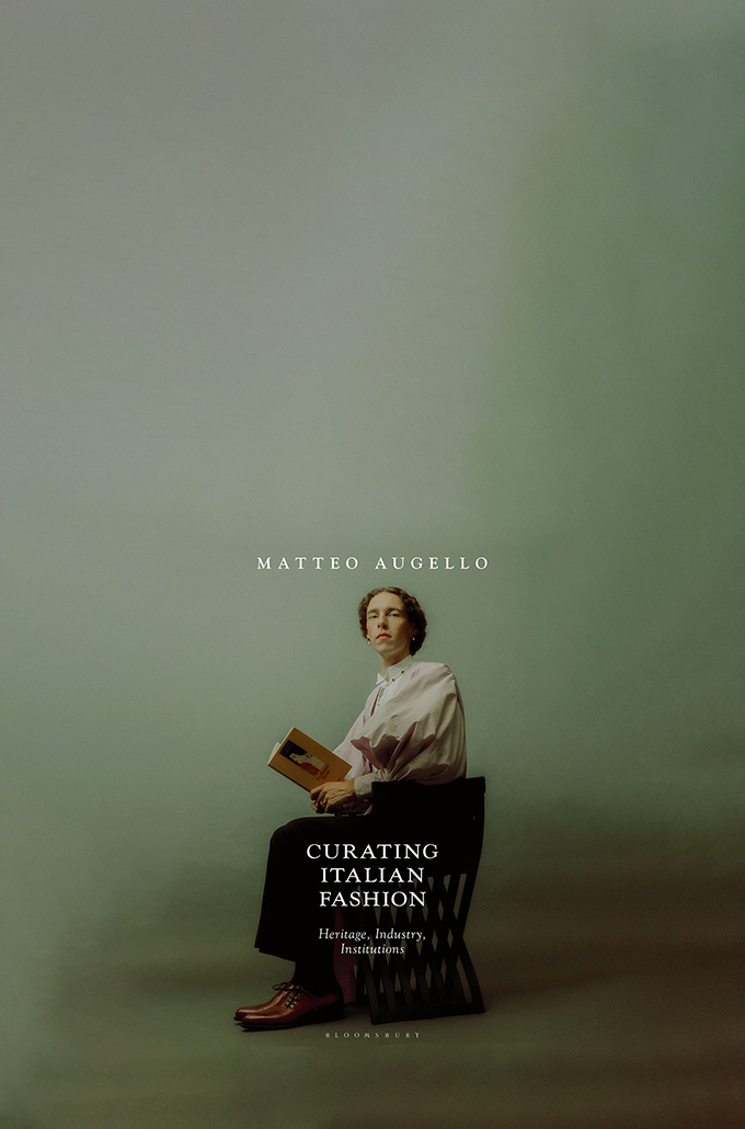 curating italian fashion book cover: a man sitting in a chair and holding a book, looking at the camera