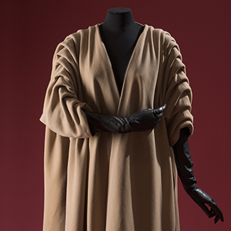 Beige swing coat on a mannequin with extra folds of fabric from shoulder to elbow