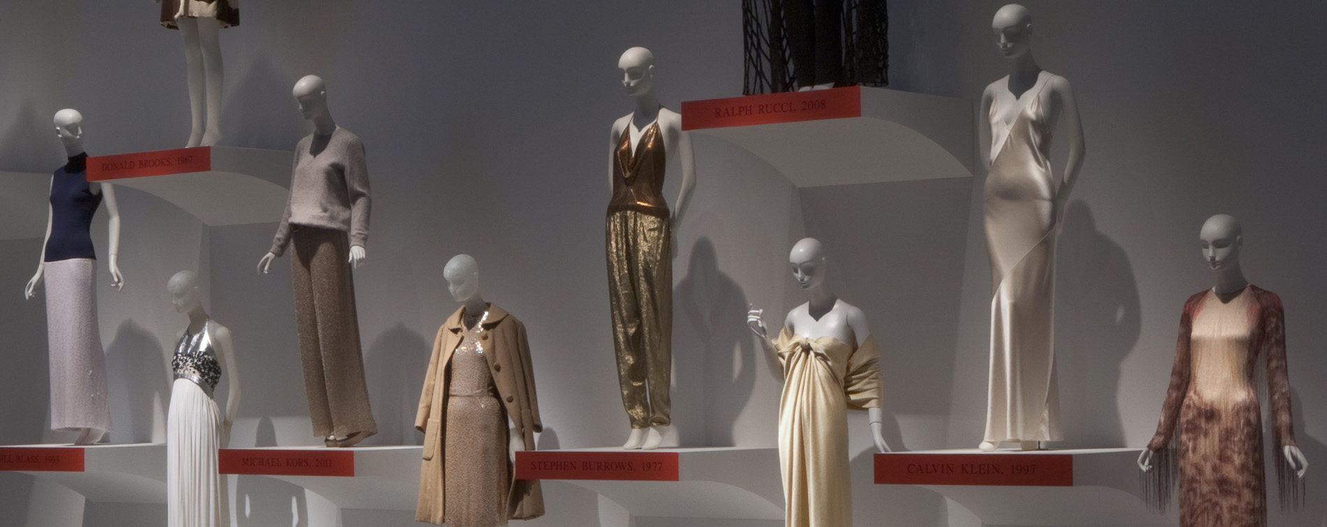 various mannequins wearing evening dresses and ensembles on platforms fixed onto a wall