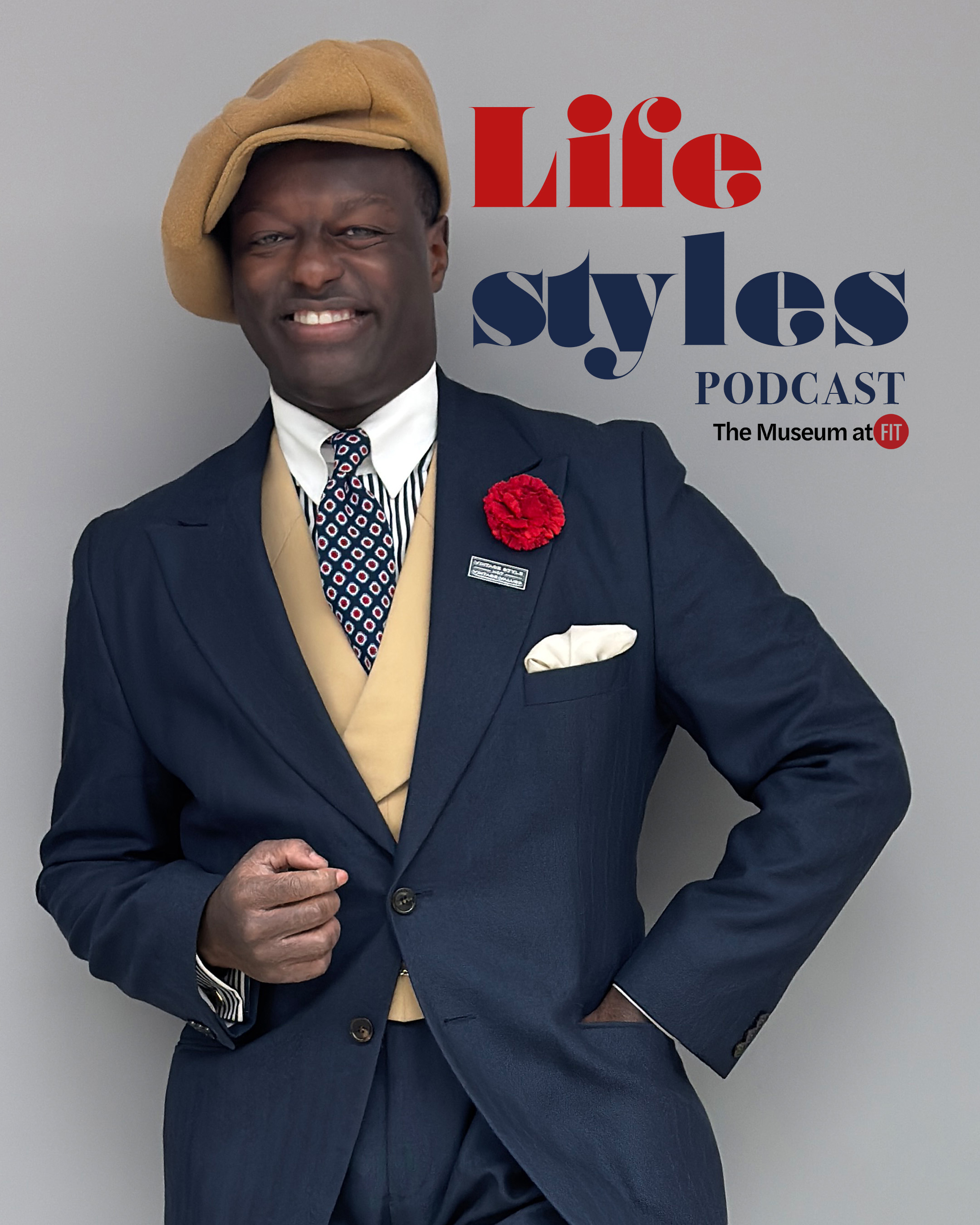 Stylish Black man waring a navy peak lapel suit styled with a red fabric carnation, white hankerchief, and small pin on the front with a tan waist coat, medallion tie, and striped button down shirt underneath, and a tan newsboy cap