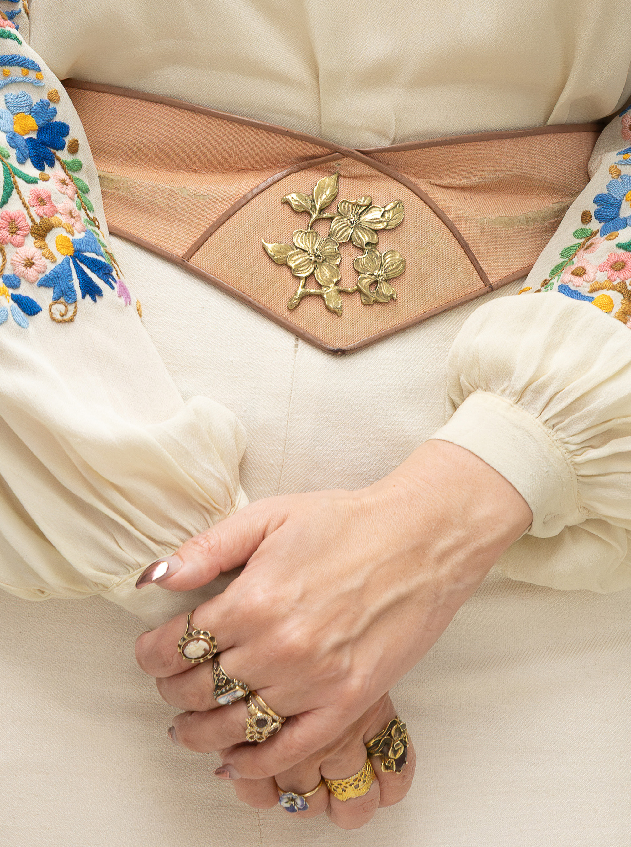close up elena's hands with various gold, antique rings and tan belt with flower detail at the center