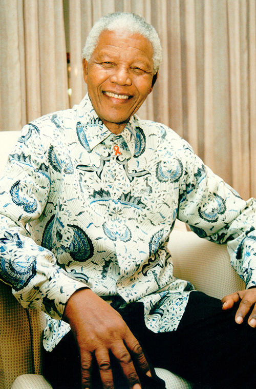 a portrait of Nelson Mandela wearing a patterned shirt sitting down and smiling