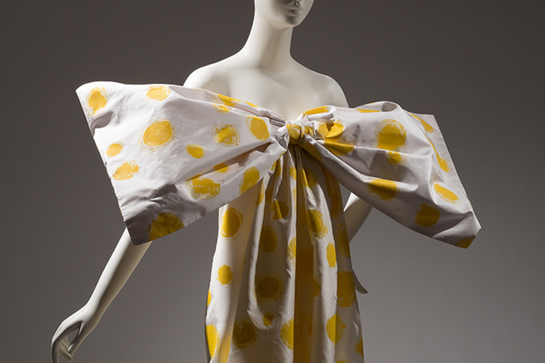 white silk dress with yellow painted polka dots and an oversized bow covering the bust