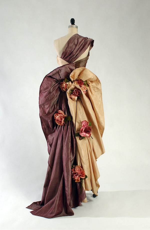 one-shoulder assymetrical evening sheath in three shades of silk shantung, rose-beige, taupe, and lavender with asymmetrically draped skirt with back twist forming bustle and swag and large silk roses scattered on back