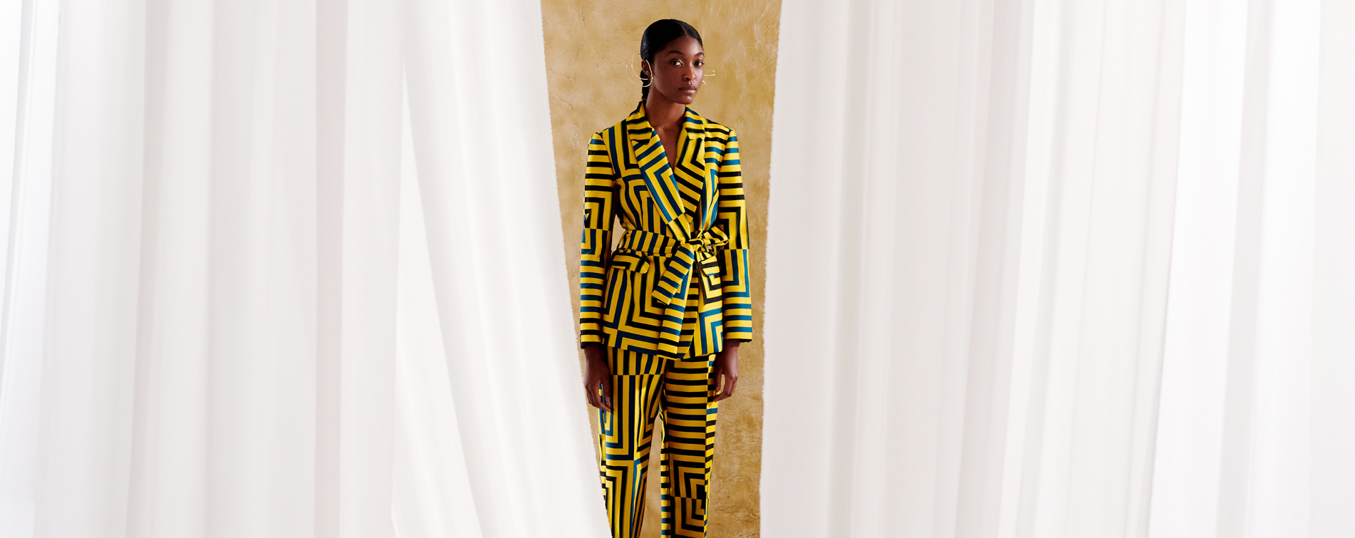 woman in yellow and black striped suit standing between white curtains