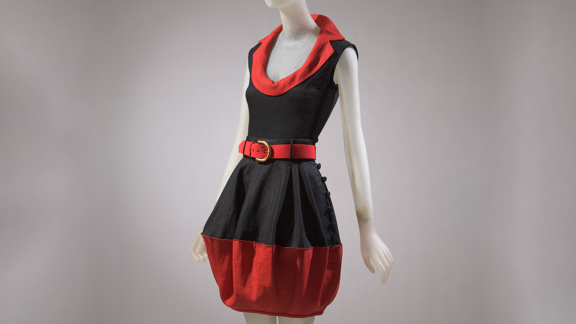 Maniquí vestida con una ensamble rojo y negro sin mangas, falda con cinturón y blusa con escote redondo