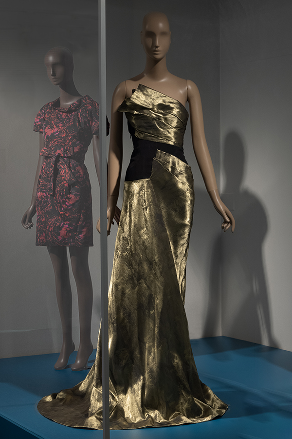 floor-length sleeveless gown in gold on a mannequin inside a gallery vitrine