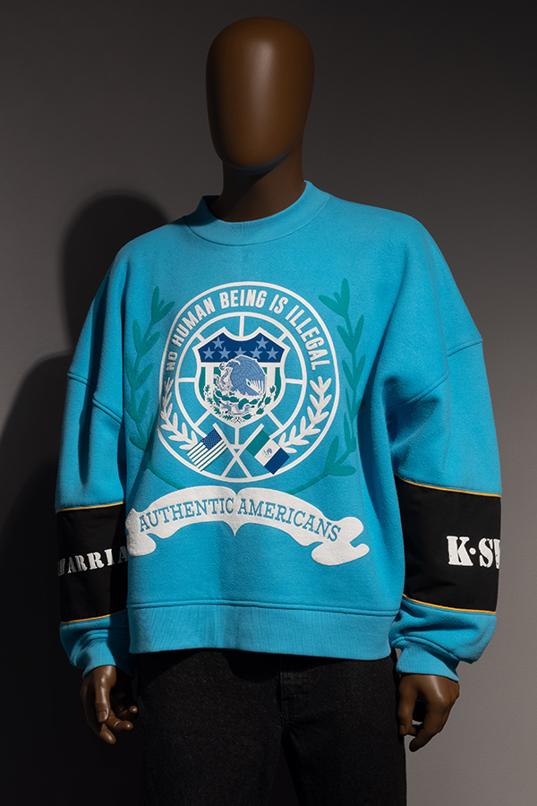 Blue oversized long-sleeved sweatshirt with an eagle, shield, flag and laurel leaf with text No Human Being is Illegal