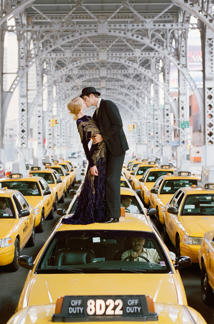 a couple kissing while standing on top of a taxi 
