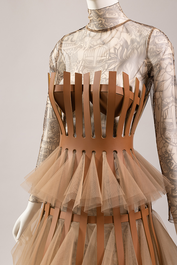 Light brown structured cage corset dress over beige tulle skirt and transparent top with tattoo patterning