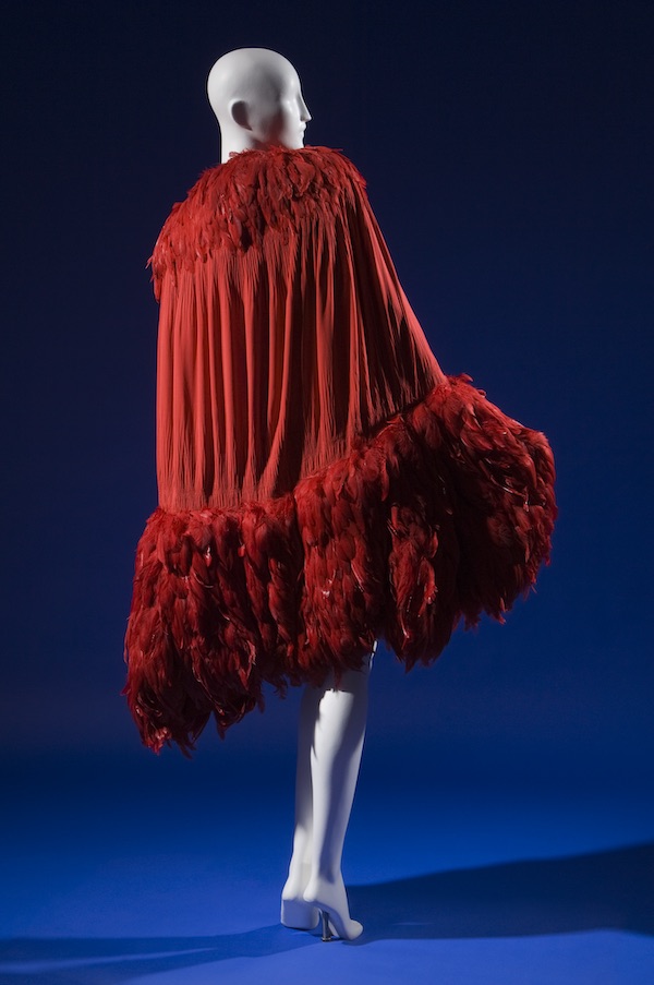 calf length evening cape in doubled red silk crepe de chine crinkled and smocked along curved edges of cocoon silhouette, crimson feather trim forming shawl collar and wide hem band