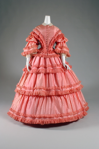 1857 full length pink dress with tiers of fringe-trimmed taffeta, corset bodice and belled sleeves