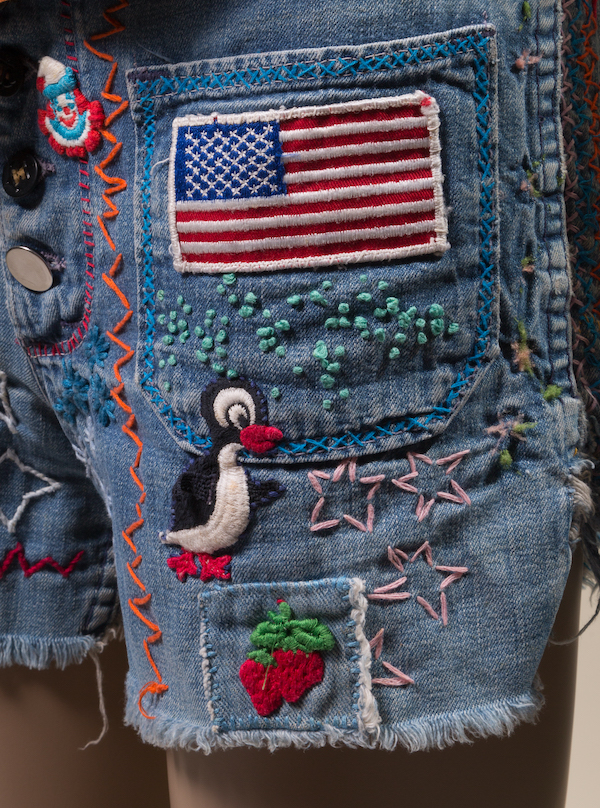 denim cut-off jeans with frayed hem, embellished embroidery and appliques overall. Designs include the America flag, a penguin, strawberries, and stars