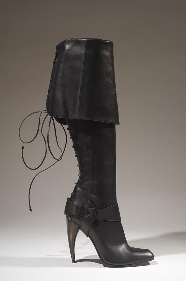 Black leather knee length pirate boots with wide cuff folded halfway down boot and curved plastic faux horn stilhetto heel; detachable black leather hoster style stirrup at ankle with snap closure; narrow squared toe; black leather tie lacing at back beginning from heel; zipper closure at instep.