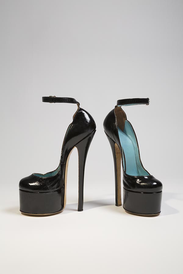Fetish platform ankle strap shoe in black patent leather; extra high spike heel, rounded toe; curved top line with two scallop points on outer edge