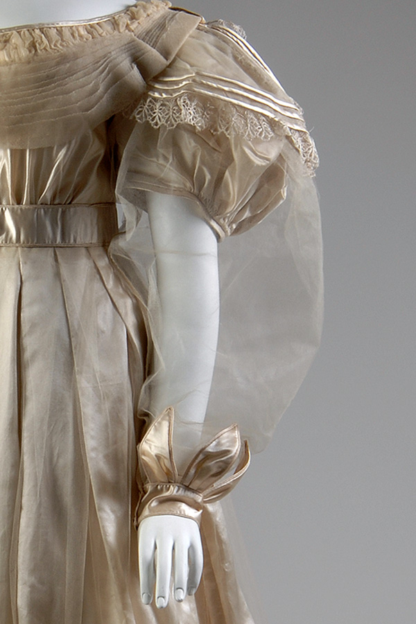 The bodice of ballgown made from cream silk satin. It has short, puffed sleeves with a long oversleeve crafted from sheer silk tulle.