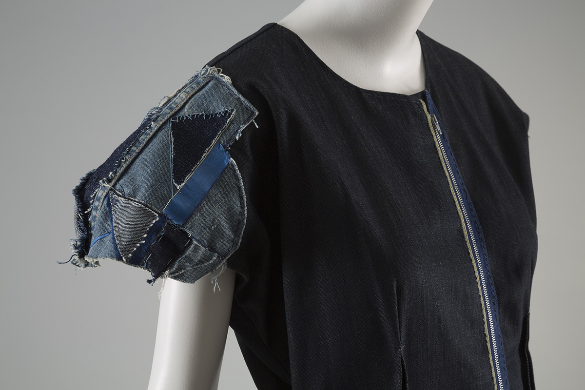 Partial front view of a denim dress with patchwork cap sleeve. 