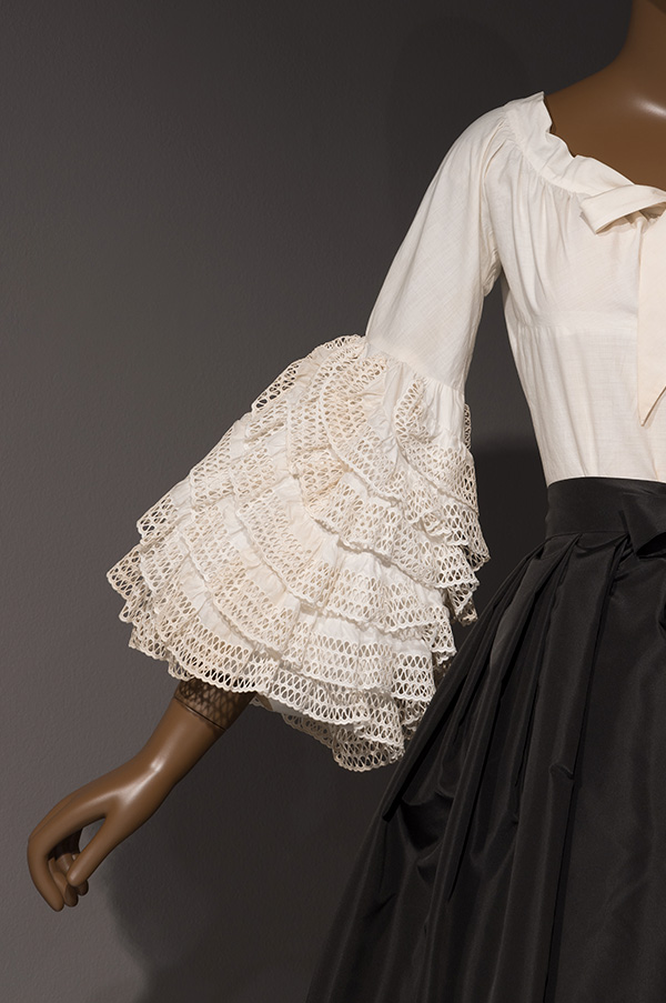 Ruffled tiers of white, lace-trimmed fabric decorate the sleeve of a white cotton blouse.