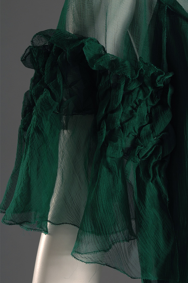 close up of sheer elbow-length sleeve with a gathered and layered decorative flounce at mid upper arm