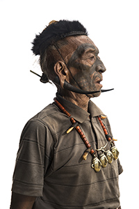 image of man with face tattoos, enlarged piercings, collared shirt and necklace staring off to the side