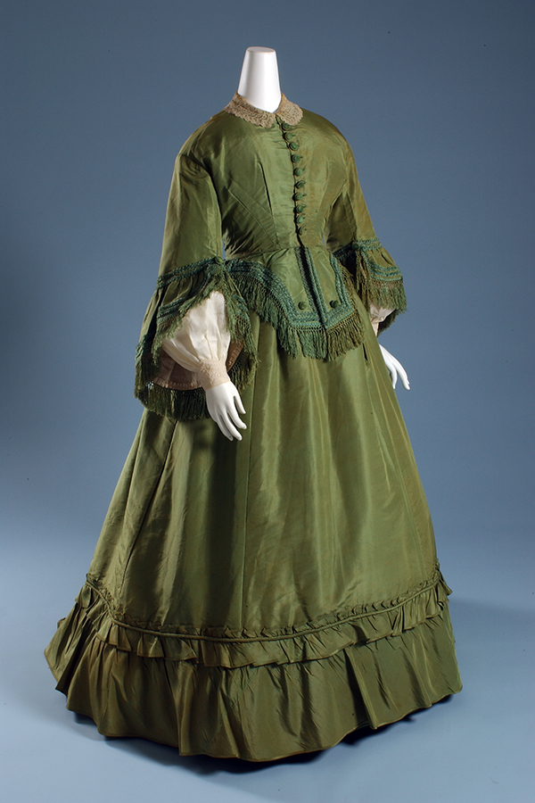 green 19th century dress with lace, soutache, and fringe on a mannequin