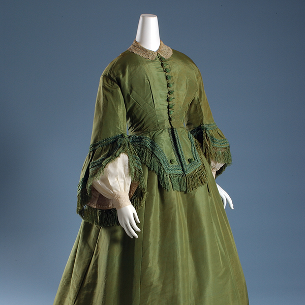 green 19th century dress with lace, soutache, and fringe on a mannequin