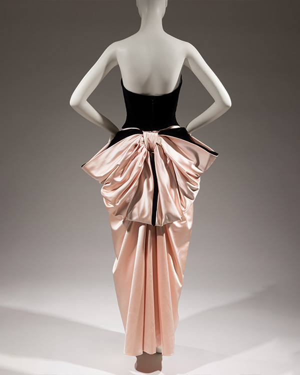 Back view of a black velvet and pink satin dress, with a large pink satin bow tied at the lower waist.