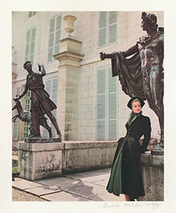 Model wearing a green dress and black coat leaning against a statue in Paris