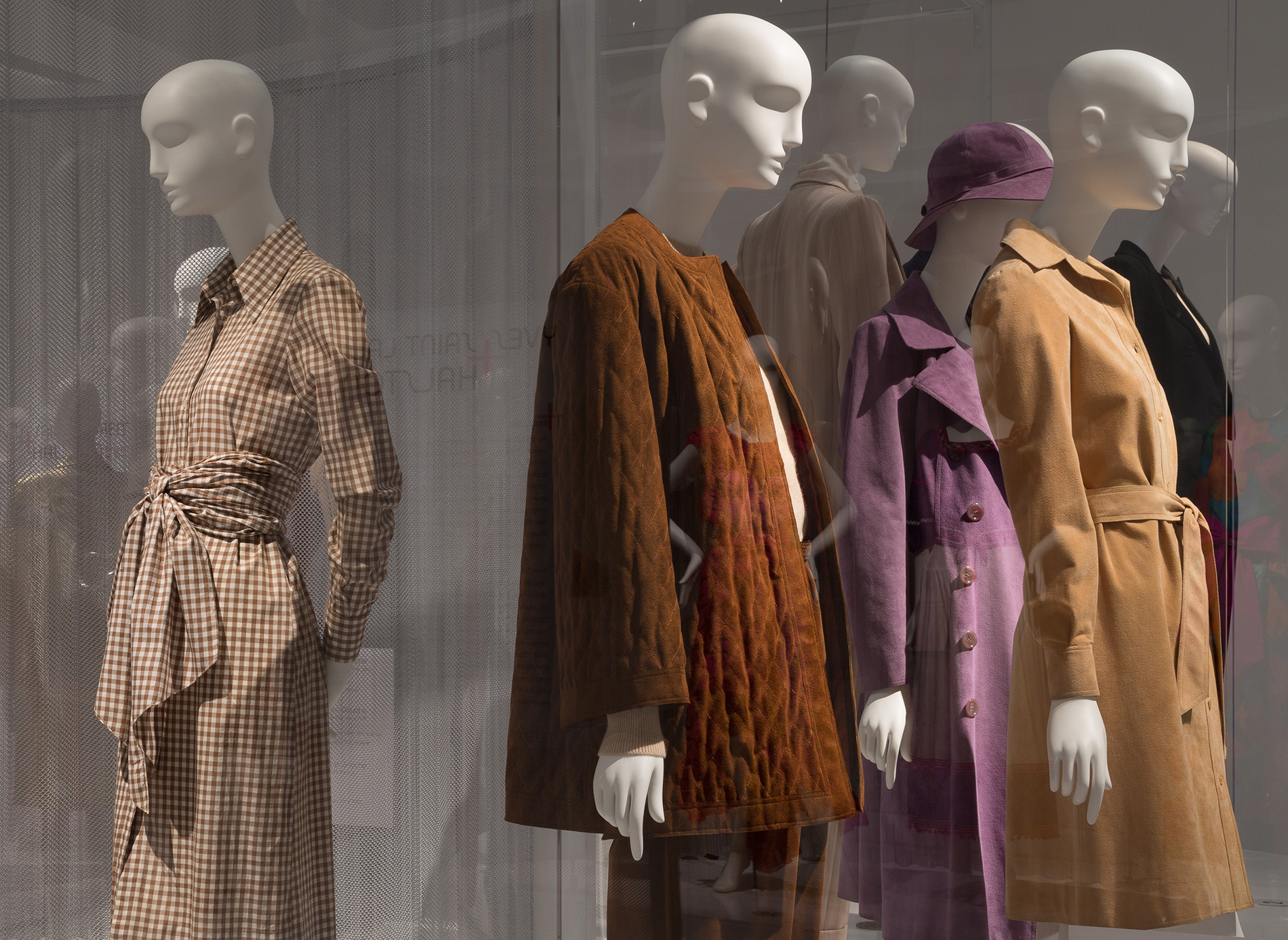 exhibition installation with several coats and ensembles on many mannequins facing away from each other