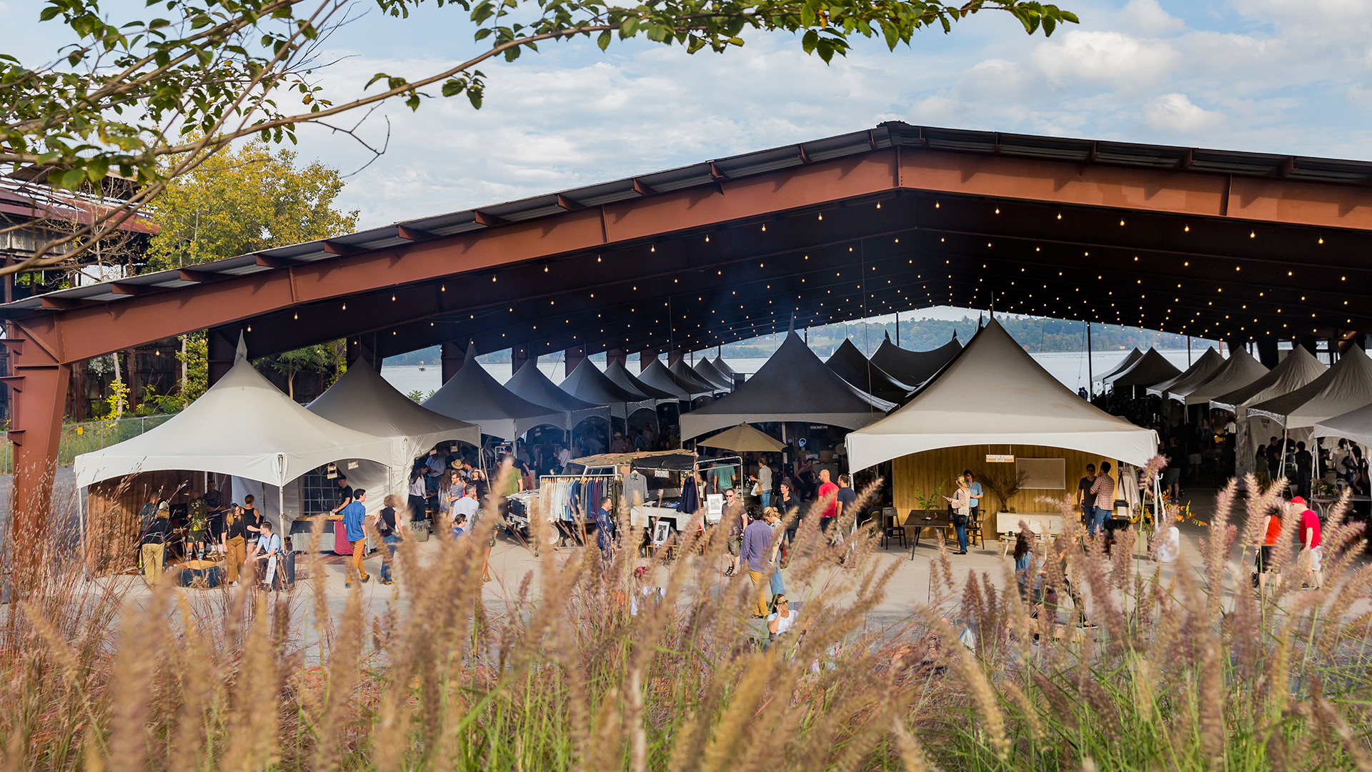 a craft market is held under an outdoor shelter, situated in a field.